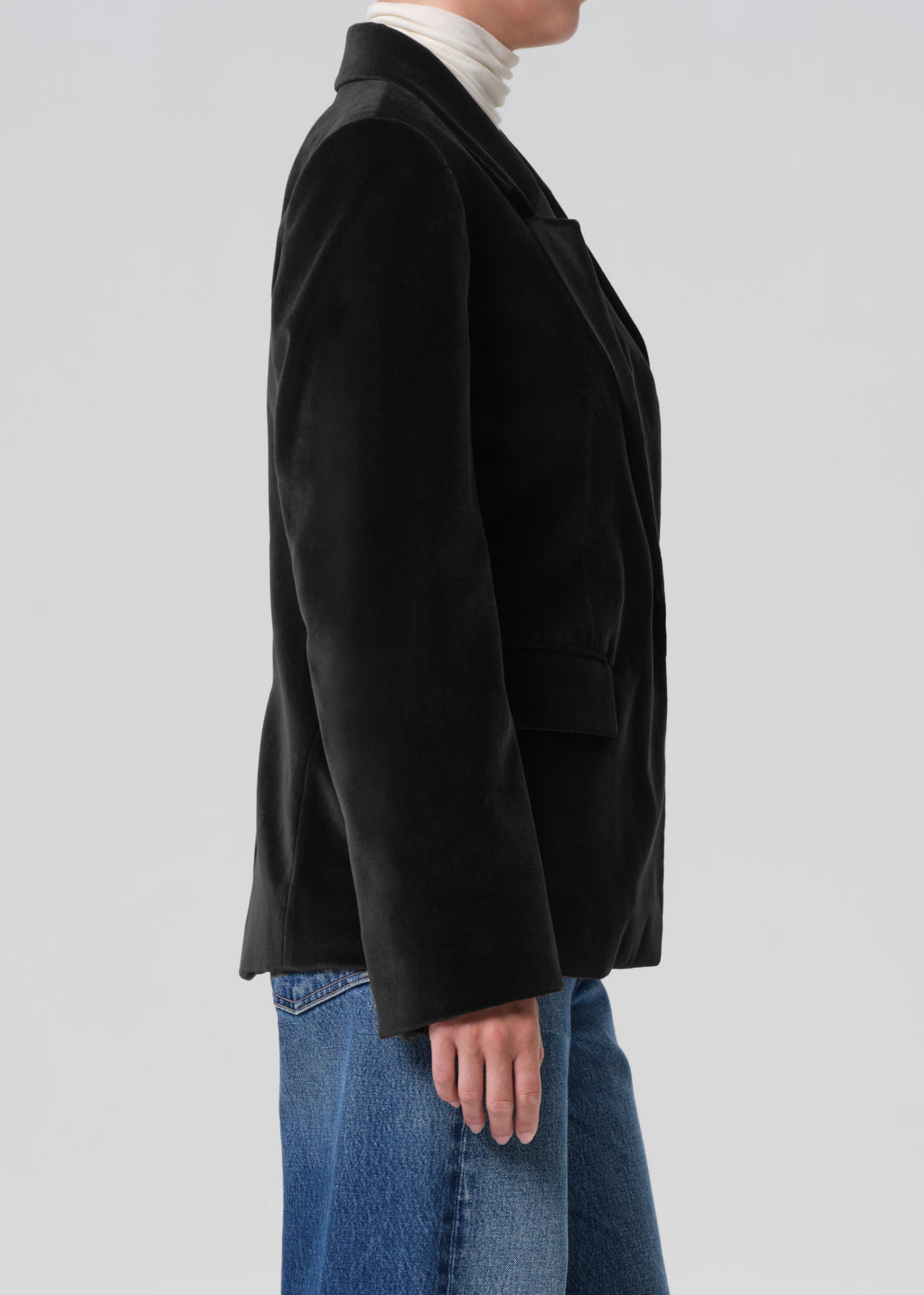 Person wearing a black coat over a white turtleneck on a light gray background