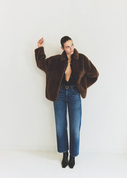 Person wearing a brown fur coat and blue jeans against a white background