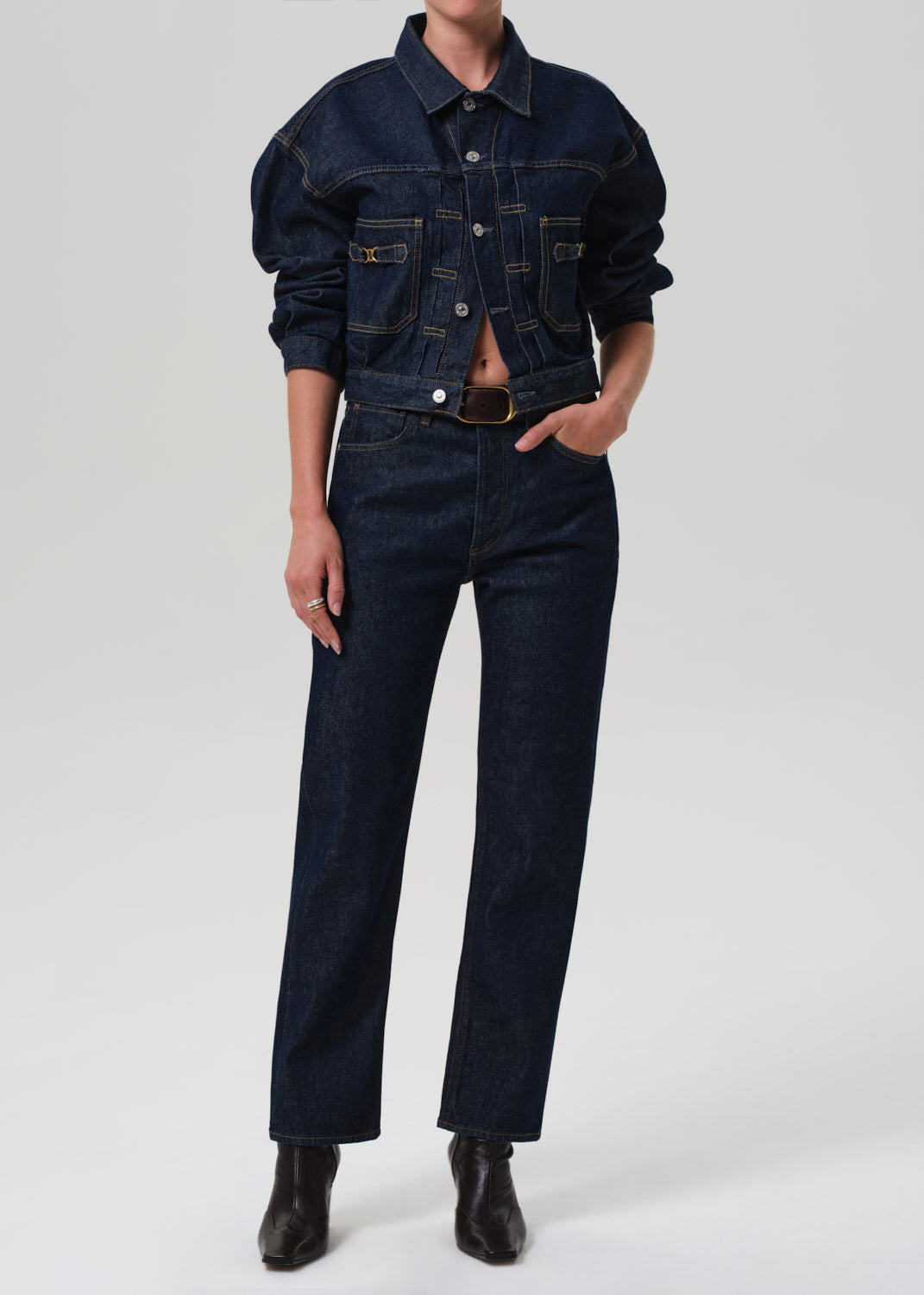 Person wearing a dark denim jacket and jeans on a grey background