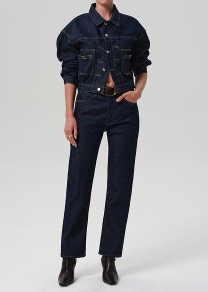 Person wearing a dark denim jacket and jeans on a grey background