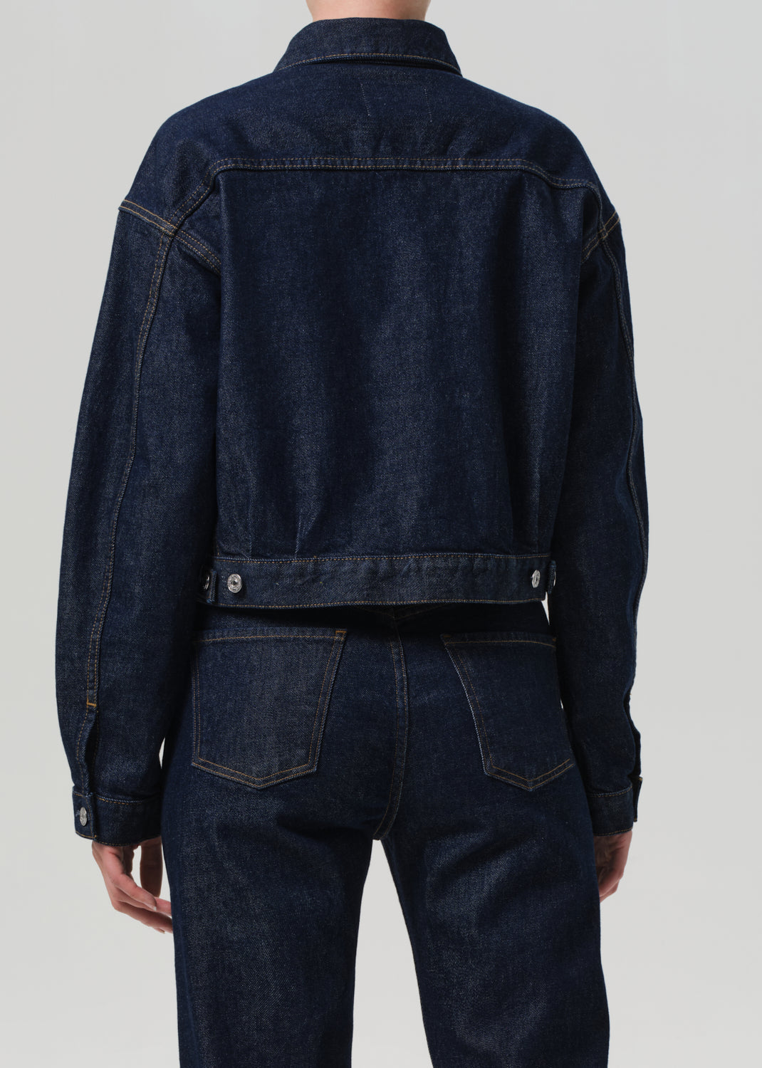 Person wearing a dark blue denim jacket and pants on a light gray background