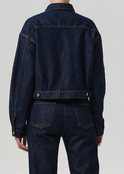 Person wearing a dark blue denim jacket and pants on a light gray background