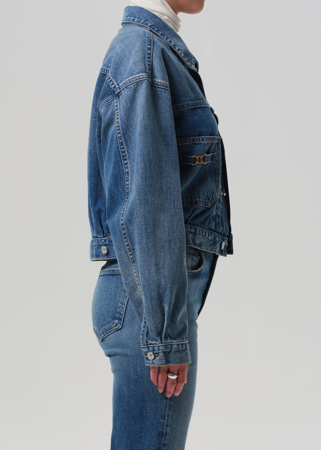 Person wearing a blue denim jacket and jeans on a light gray background