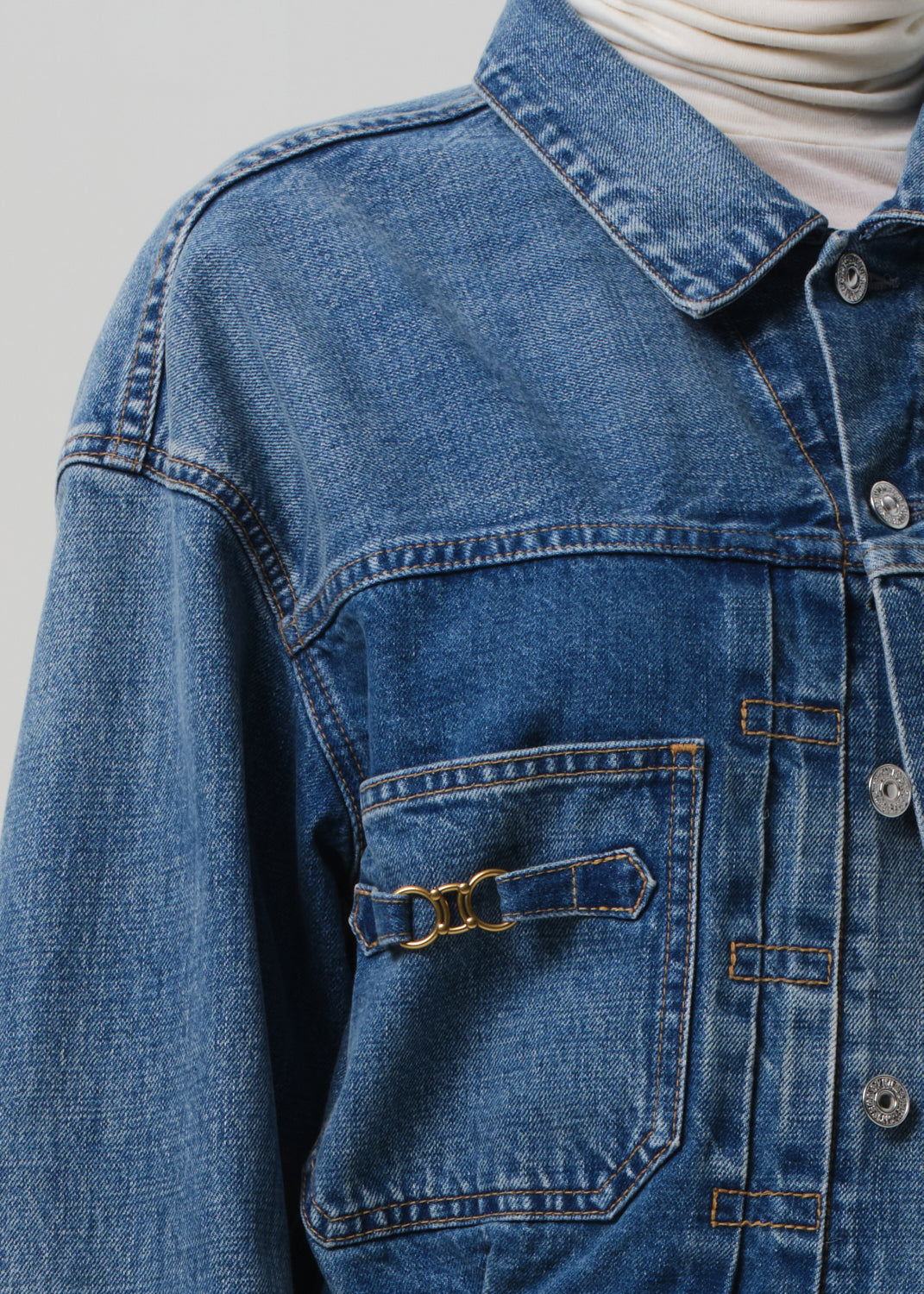 Close-up of a blue denim jacket with a buckle detail on a gray background