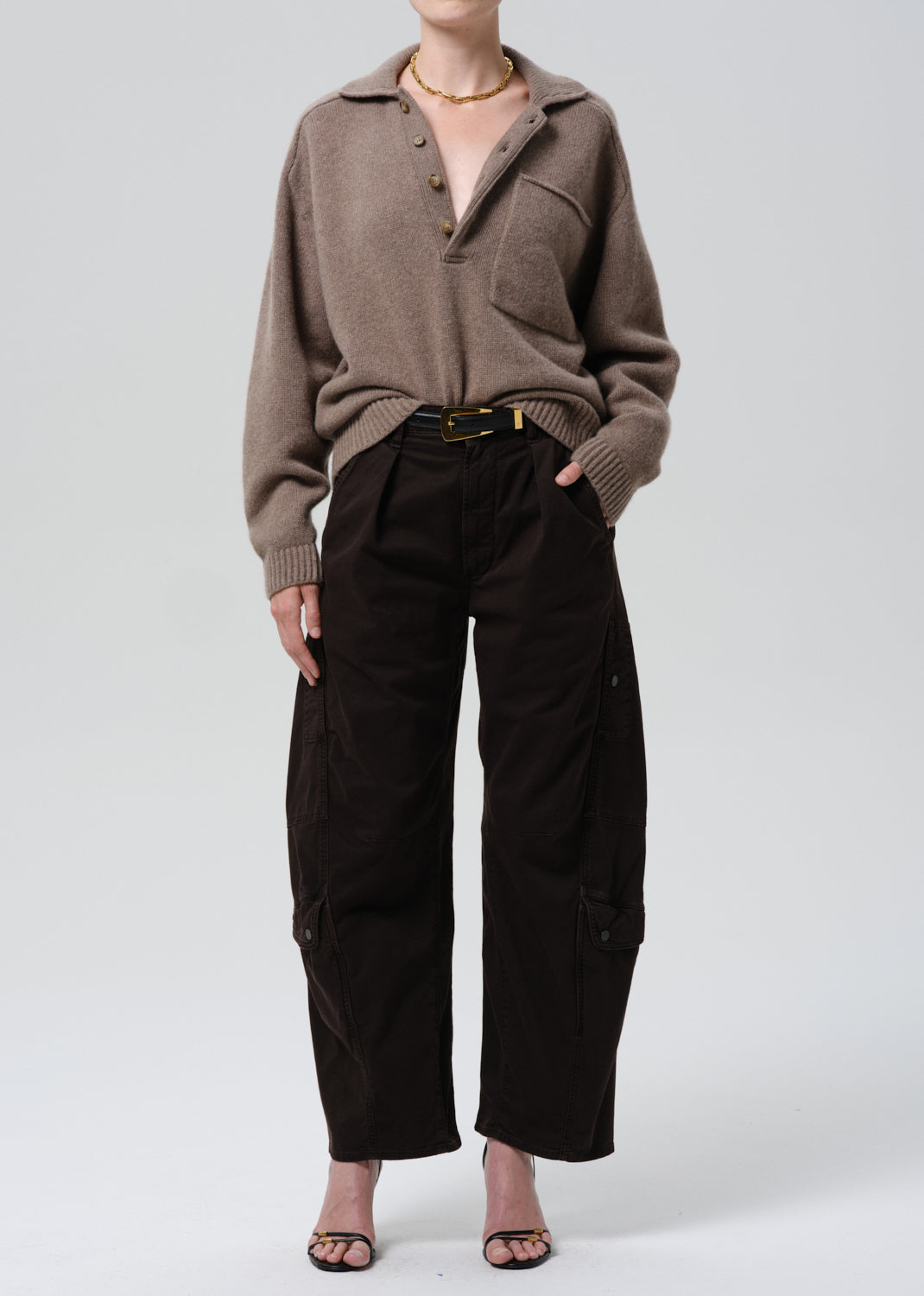 Person wearing a brown sweater and black pants on a grey background