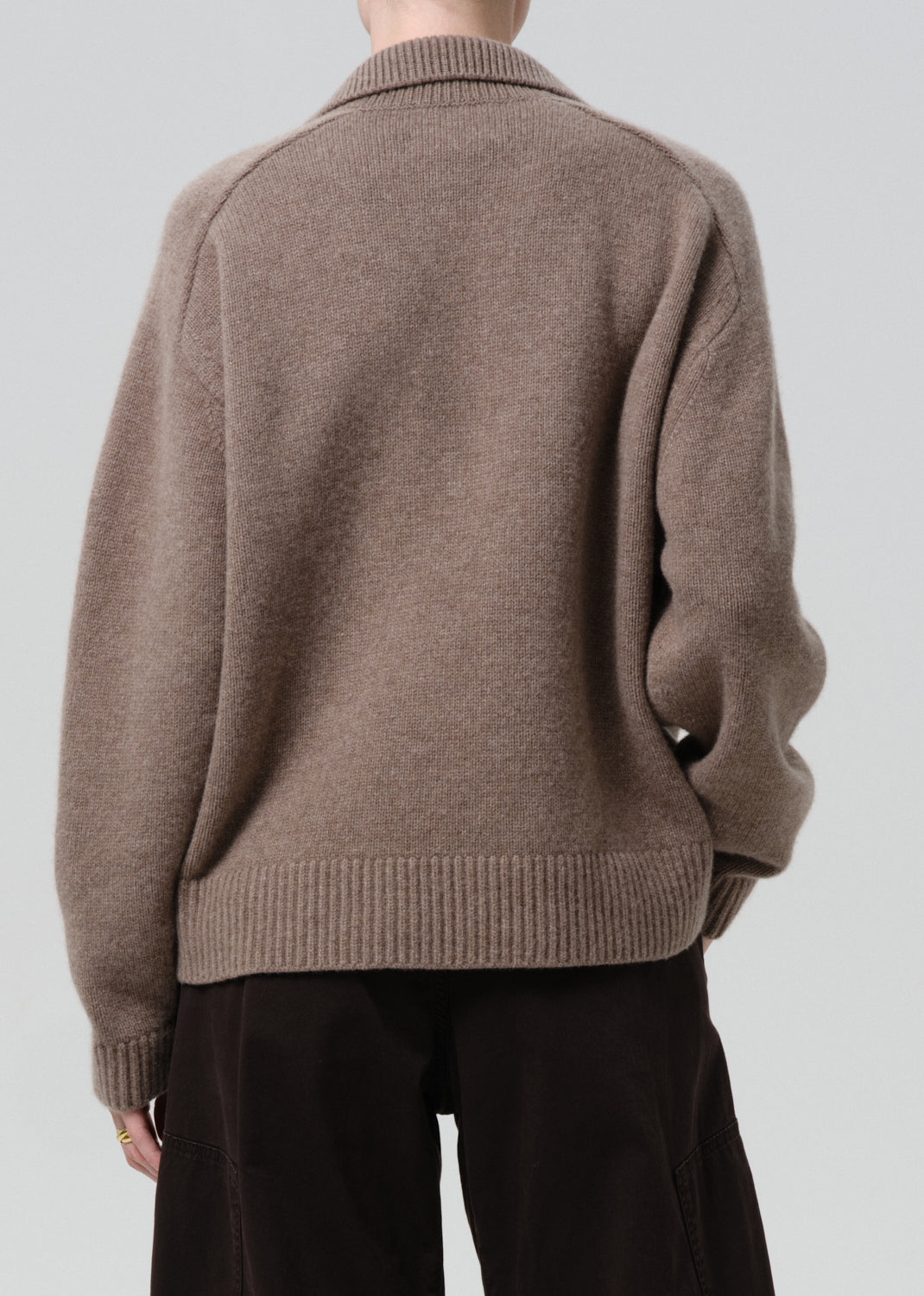 Person wearing a brown sweater against a grey background