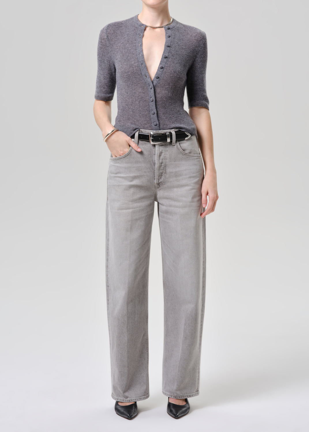 Person wearing a gray cardigan and light gray pants on a grey background.