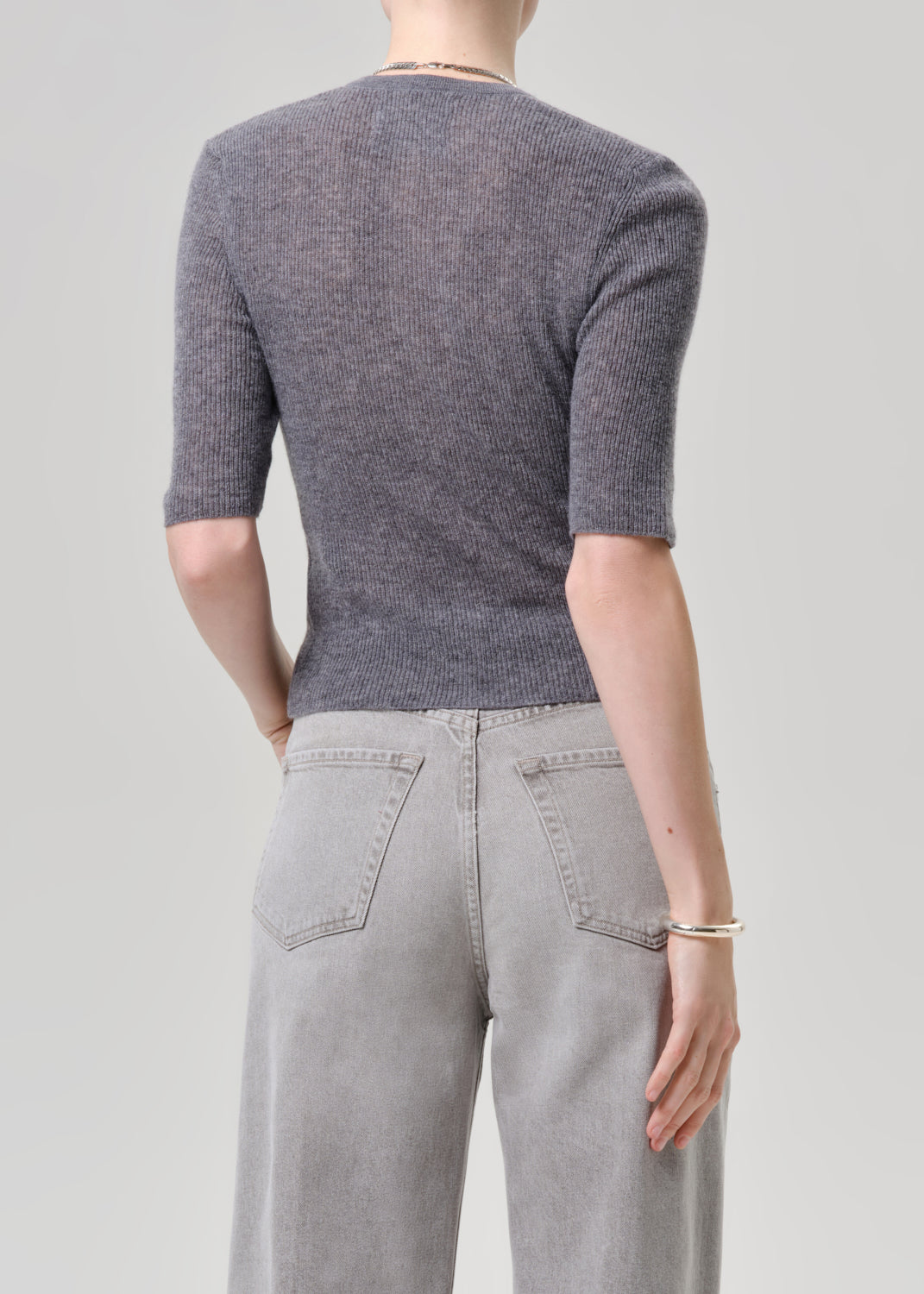 A model shown from the back wearing a dark grey ribbed short-sleeve knit top and light grey wide-leg jeans against a solid light grey background.