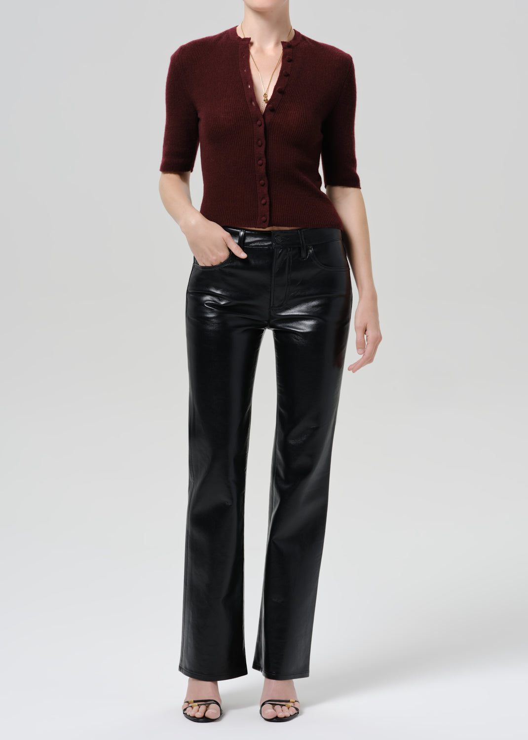 Person wearing burgundy cardigan and black pants on a grey background