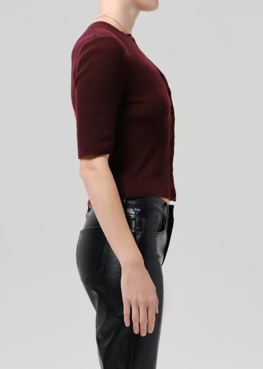 Person wearing burgundy cardigan and black pants on a grey background