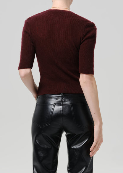 Person wearing burgundy cardigan and black pants on a grey background