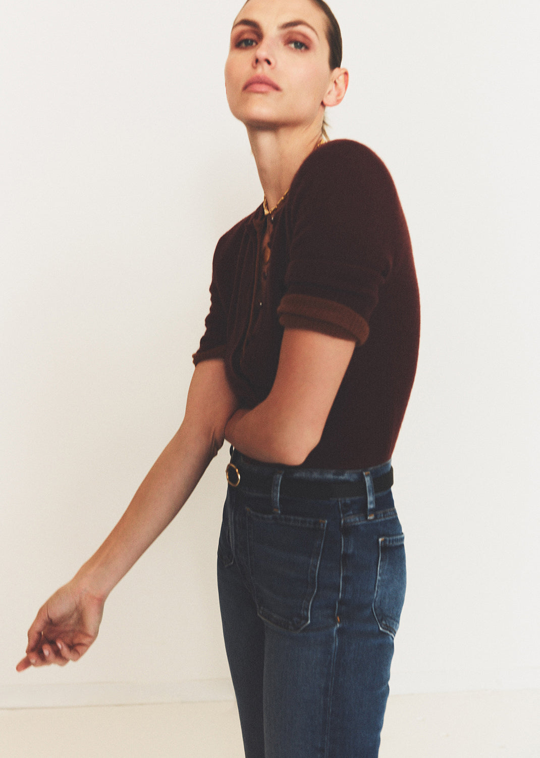 Woman wearing a brown top and blue jeans against a plain background