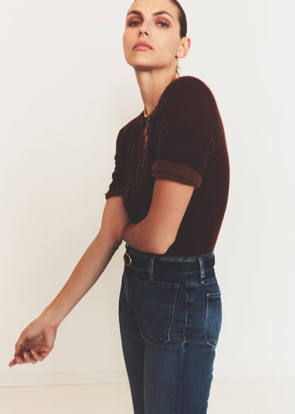 Woman wearing a brown top and blue jeans against a plain background