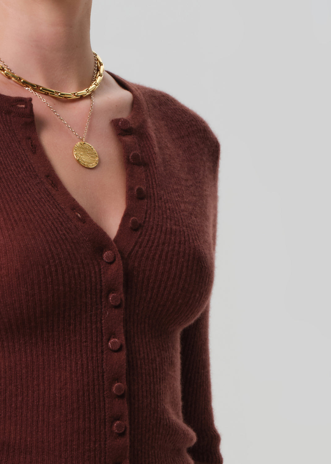 Brown cardigan worn by a person with gold jewelry on a light gray background