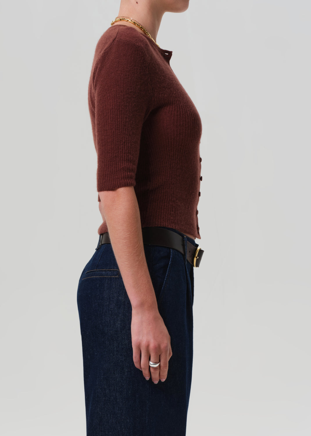 Person wearing a brown sweater and dark jeans on a light gray background