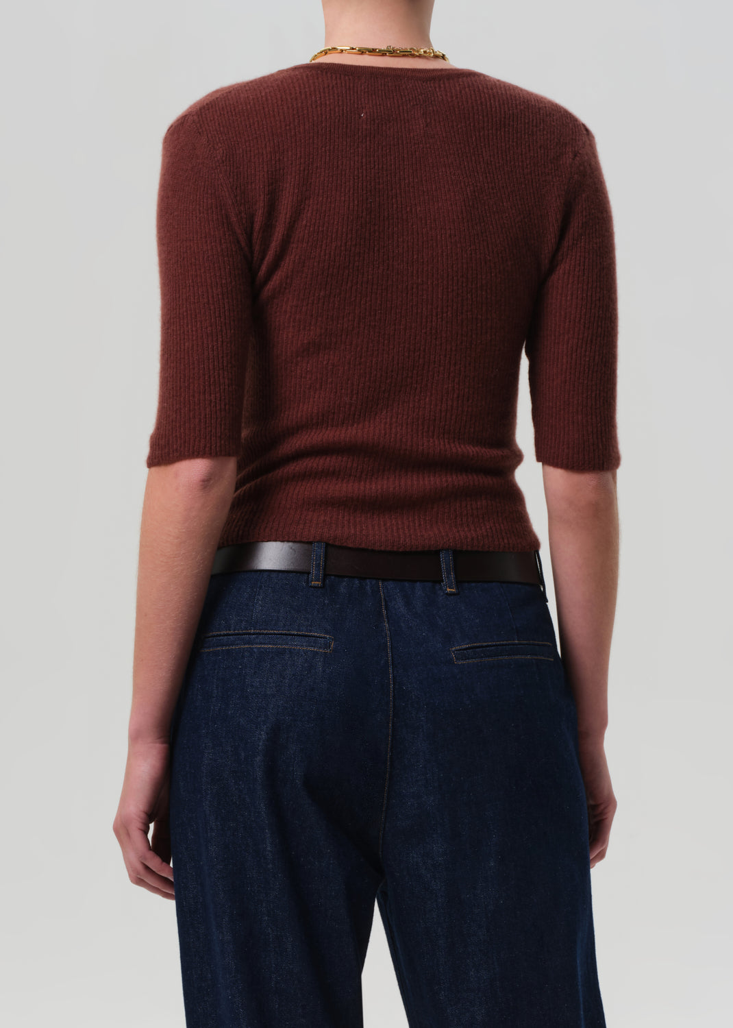 Person wearing a brown ribbed sweater and dark blue jeans on a plain background