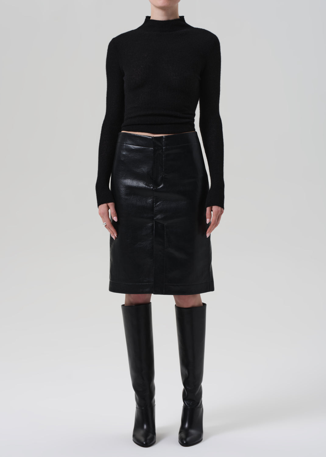 Person wearing a black turtleneck, black leather skirt, and black knee-high boots on a white background