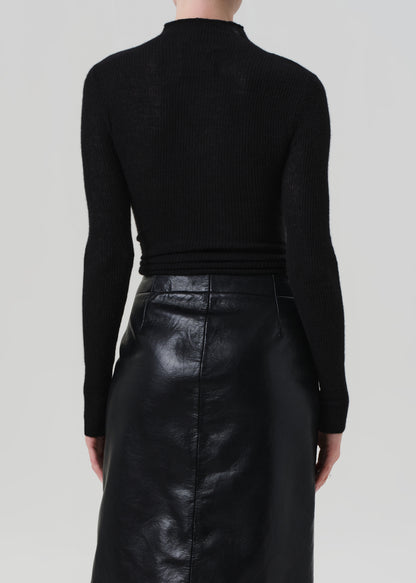 Person wearing a black turtleneck sweater and black leather skirt on a light gray background