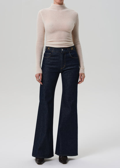 Person wearing a beige turtleneck and dark blue flared jeans on a white background