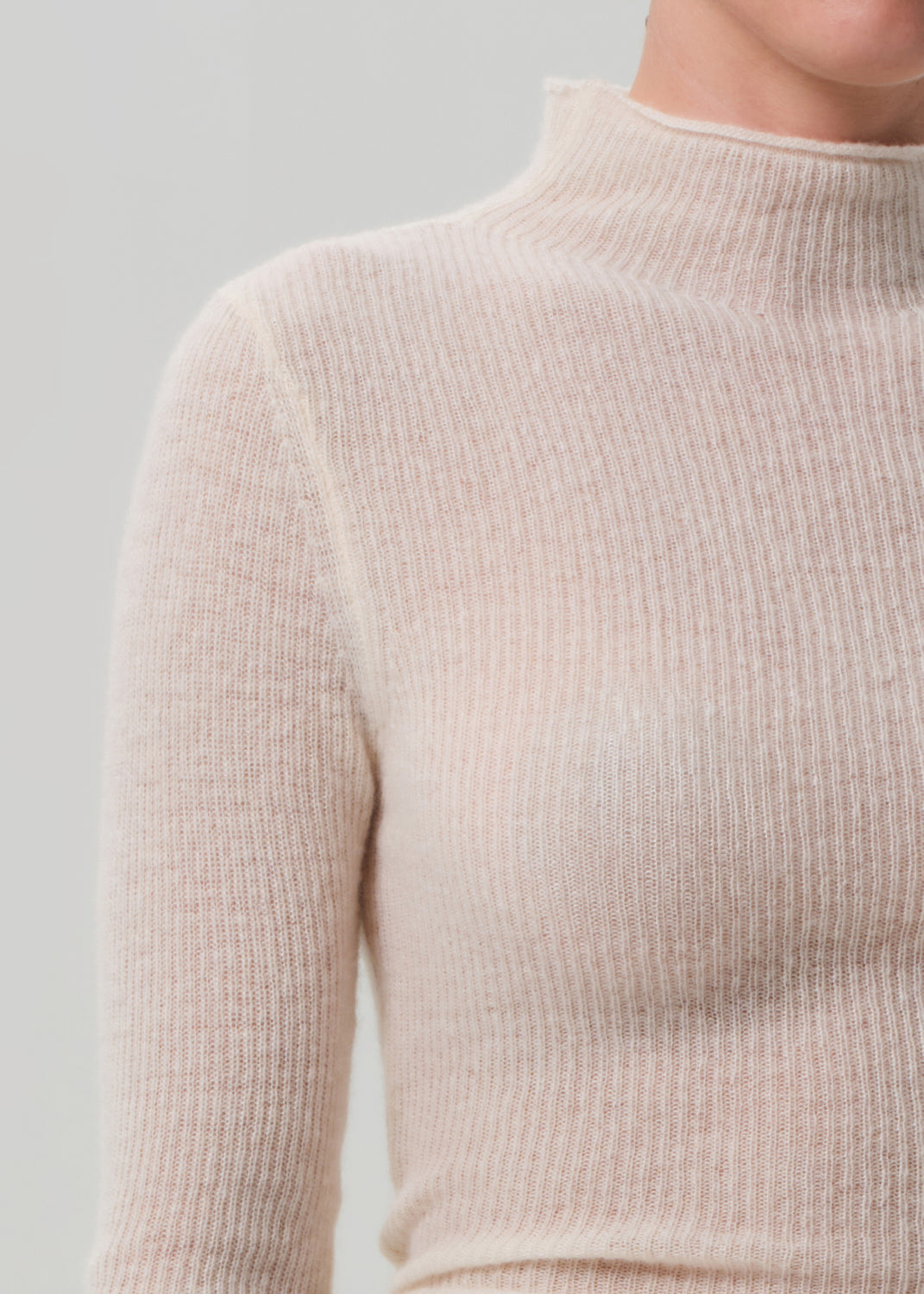 Close-up of a person wearing a beige ribbed sweater against a light gray background