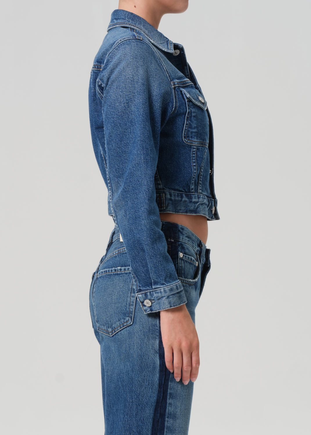 Person wearing a blue denim jacket and jeans on a light gray background