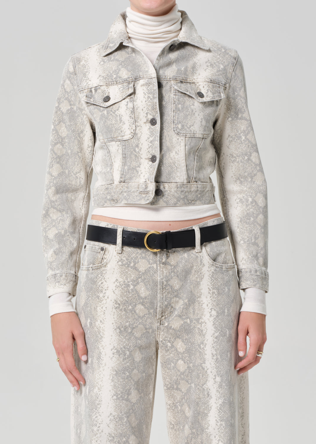Person wearing a python patterned denim jacket and jean with a belt on a plain background