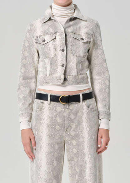 Person wearing a python patterned denim jacket and jean with a belt on a plain background