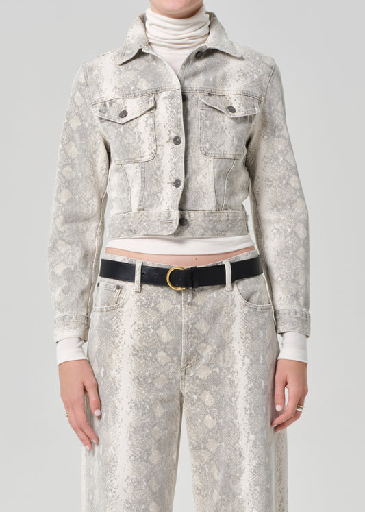 Person wearing a python patterned denim jacket and jean with a belt on a plain background