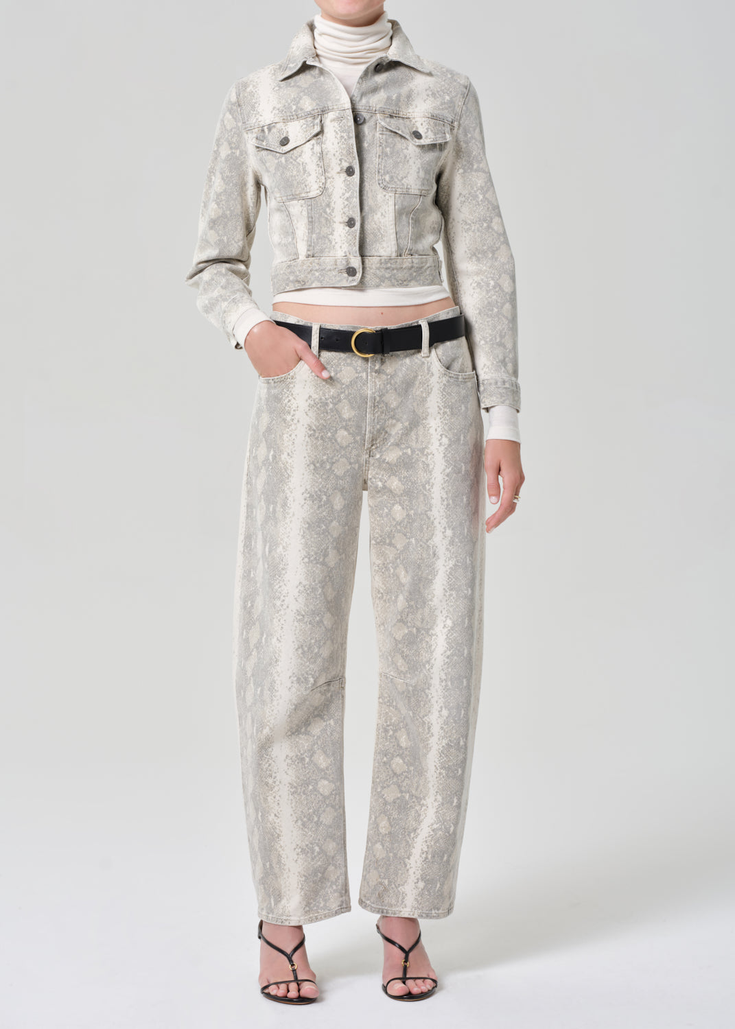 Person wearing a python patterned denim jacket and jean with a belt on a plain background