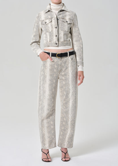 Person wearing a python patterned denim jacket and jean with a belt on a plain background