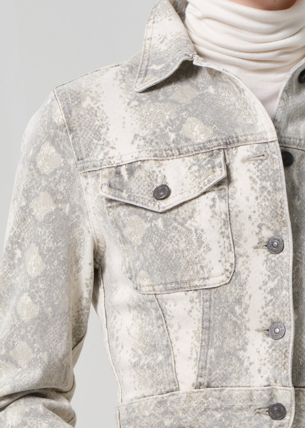 Person wearing a python patterned denim jacket and jean with a belt on a plain background