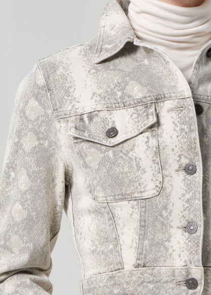 Person wearing a python patterned denim jacket and jean with a belt on a plain background