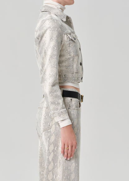 Person wearing a python patterned denim jacket and jean with a belt on a plain background