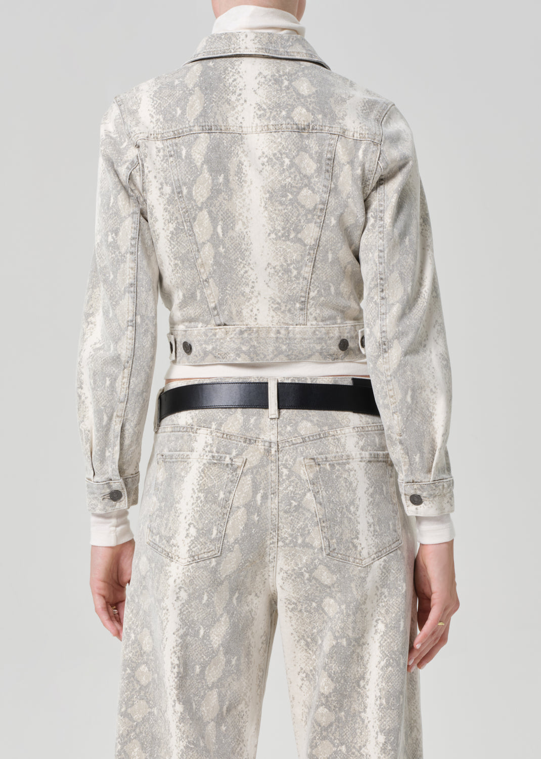 Person wearing a python patterned denim jacket and jean with a belt on a plain background