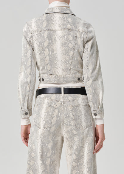 Person wearing a python patterned denim jacket and jean with a belt on a plain background