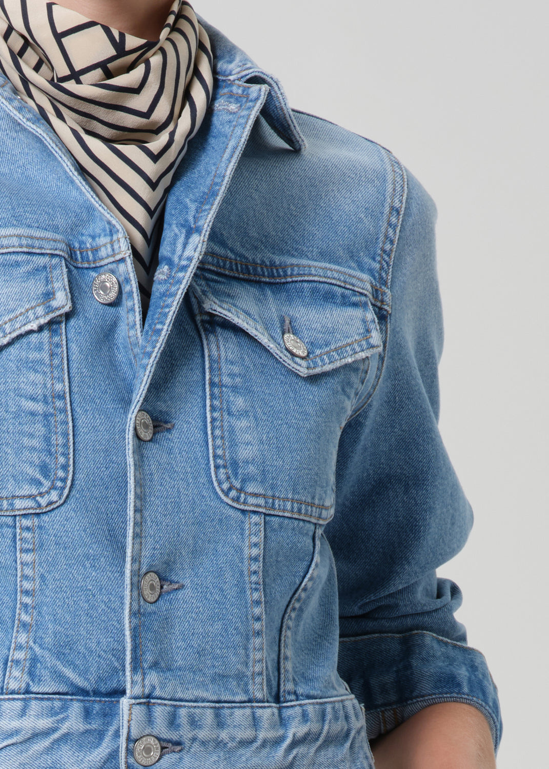 Person wearing a blue denim jacket with a striped scarf on a plain background