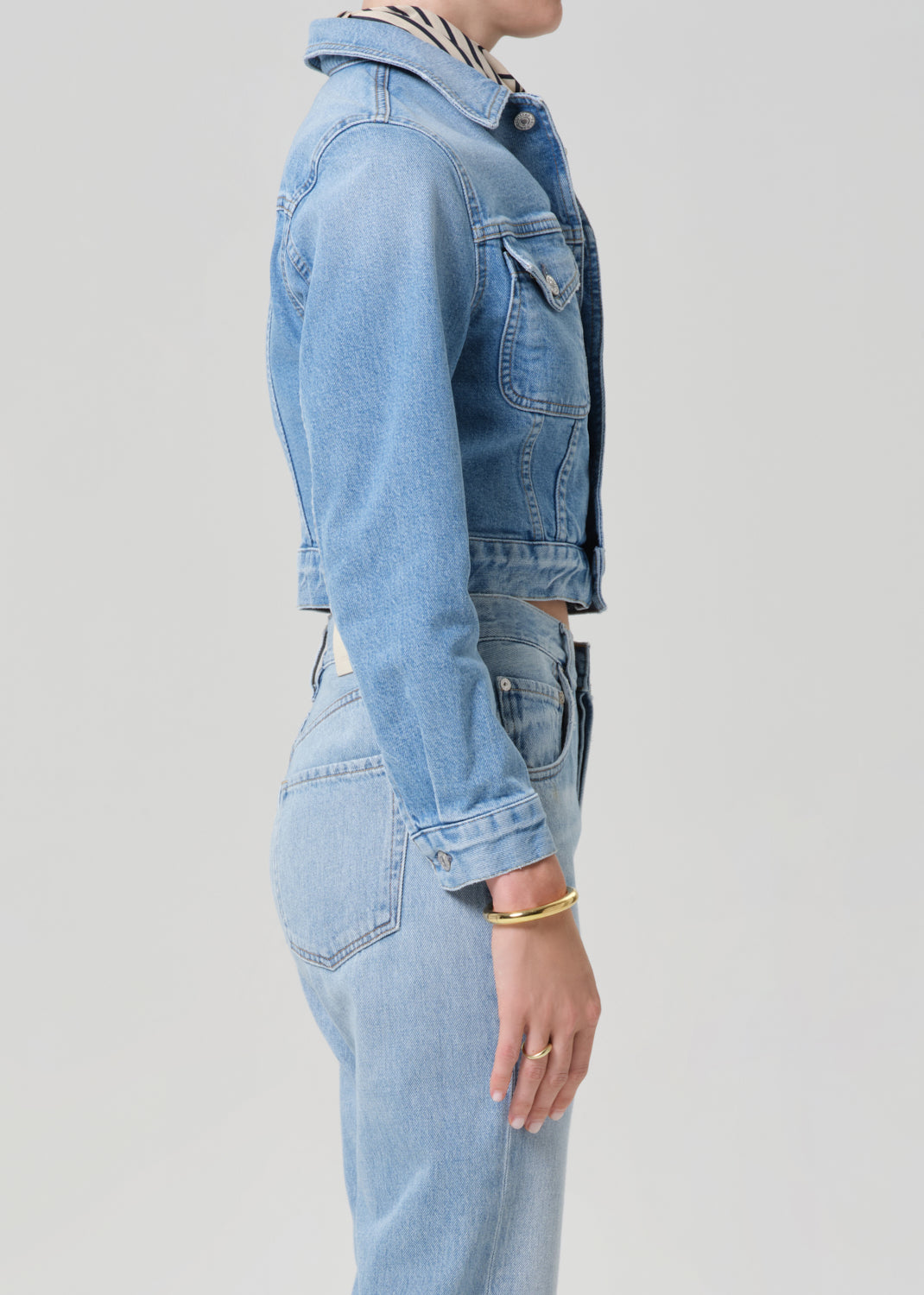 Person wearing a light blue denim jacket and jeans on a plain background