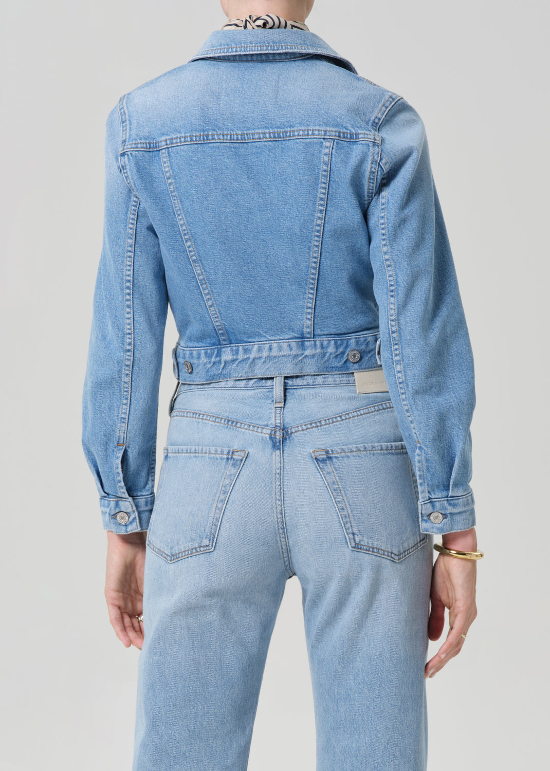 Person wearing a denim jacket and jeans on a plain background