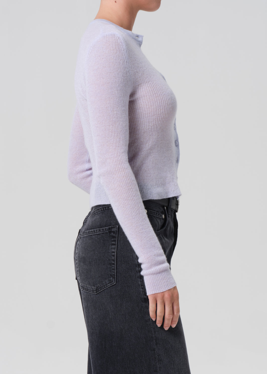 Person wearing a light blue ribbed sweater and dark jeans on a plain background