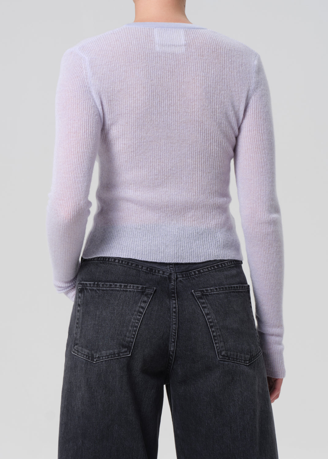 Person wearing a light blue ribbed sweater and dark jeans on a plain background