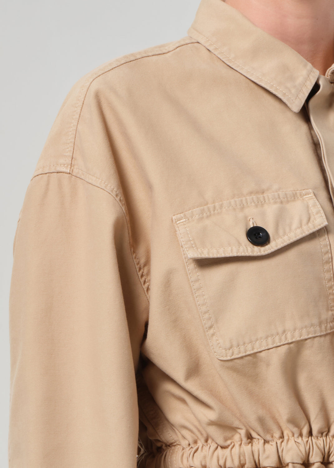 Close-up of a beige jacket with a pocket and button on a light gray background