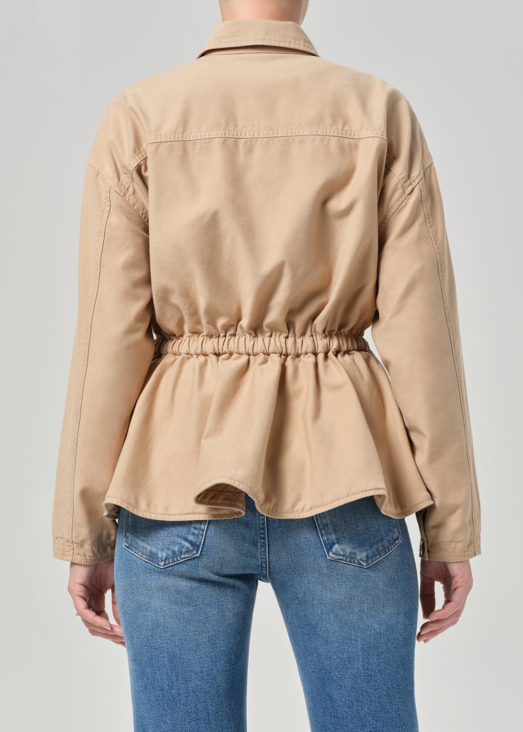 Person wearing a beige jacket and blue jeans on a plain background