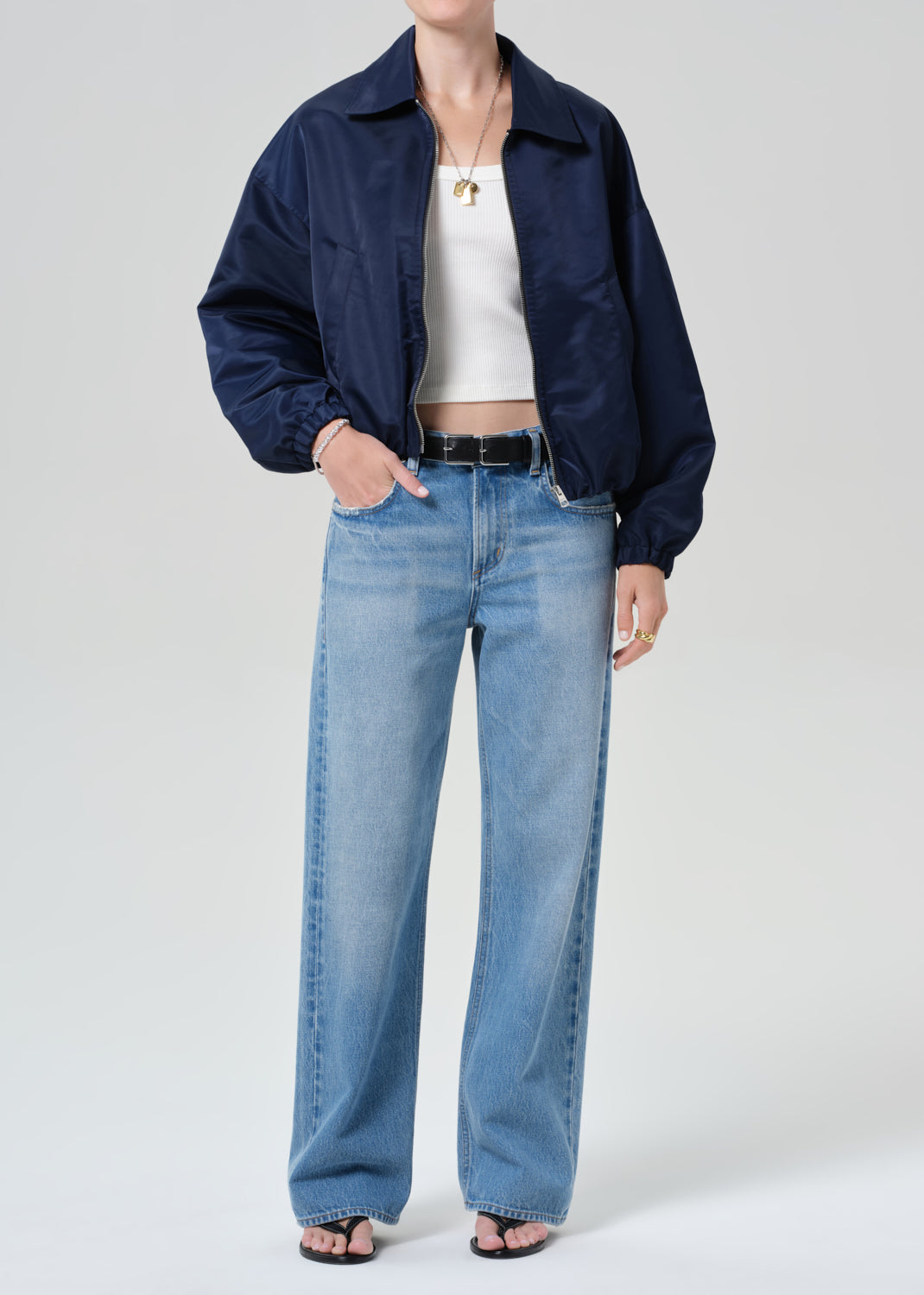 Person wearing a navy jacket, white top, and blue jeans on a plain background