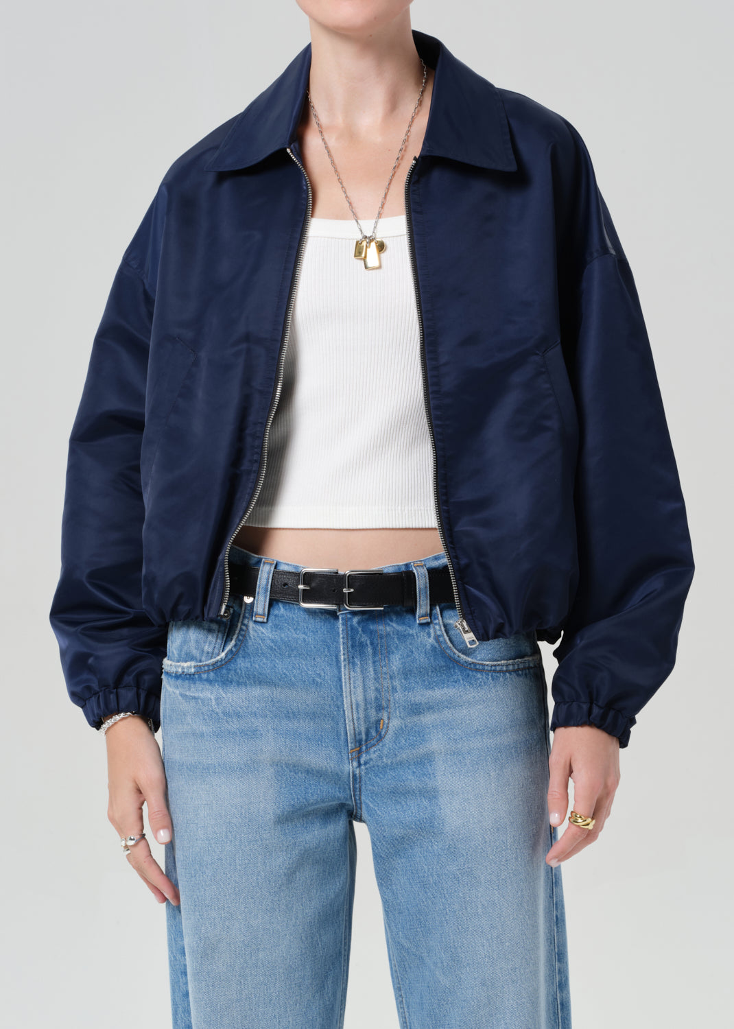 Person wearing a navy jacket, white top, and blue jeans on a plain background