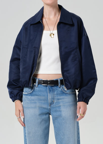 Person wearing a navy jacket, white top, and blue jeans on a plain background