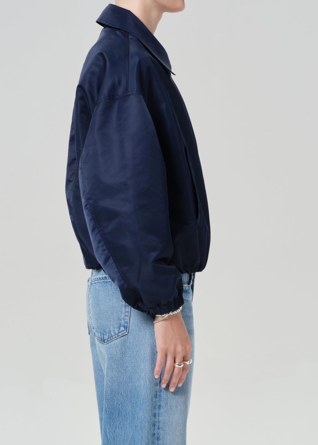 Person wearing a navy jacket and light blue jeans on a plain background