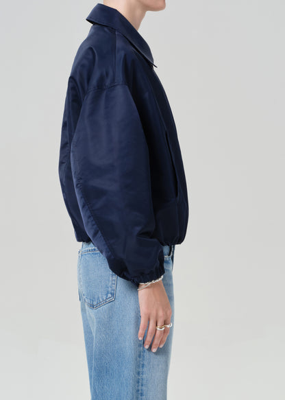 Person wearing a navy jacket and light blue jeans on a plain background