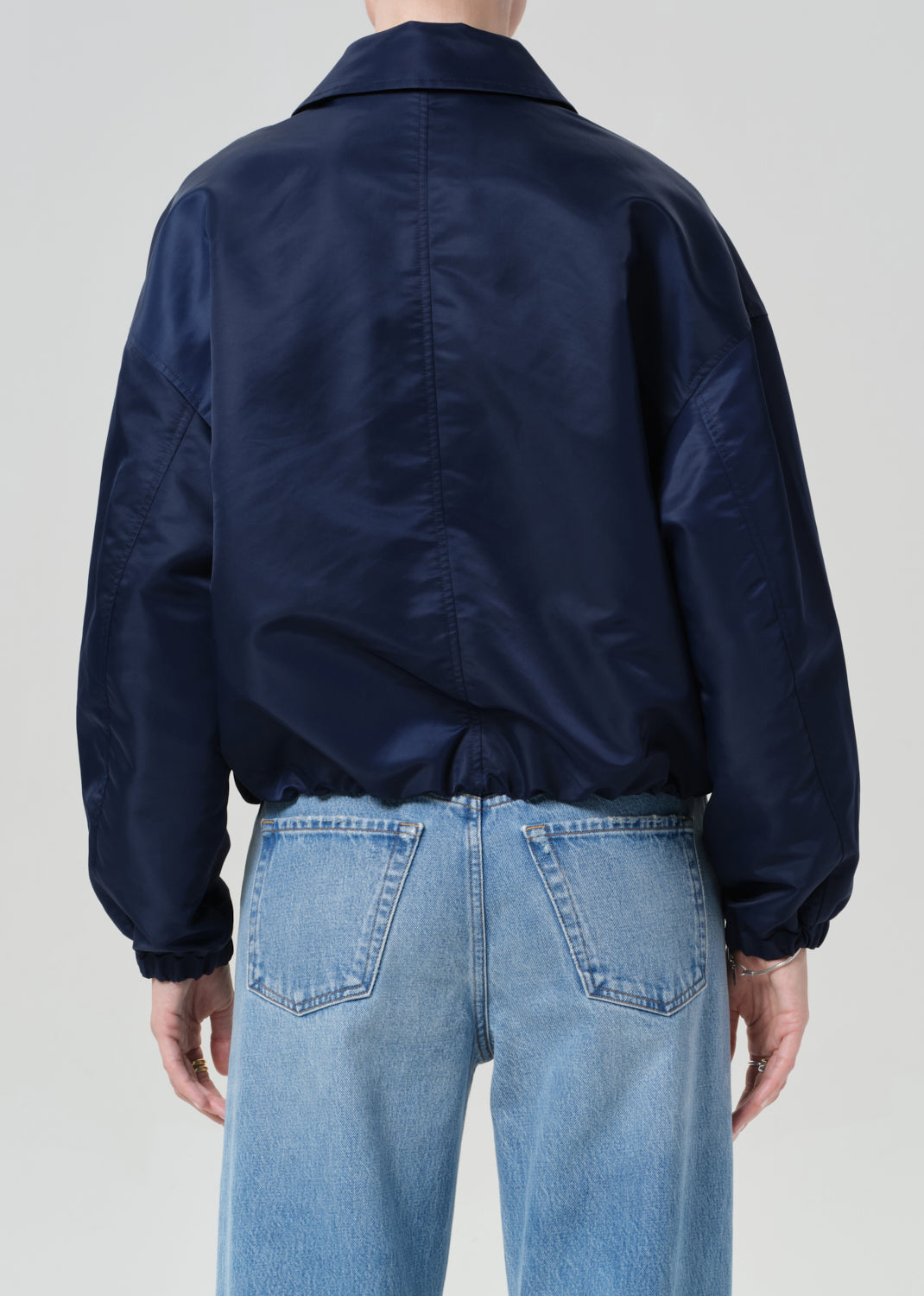 Person wearing a navy jacket and light blue jeans on a plain background