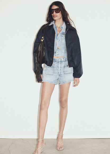 Woman wearing a denim jacket, shirt, and shorts with sunglasses on a white background