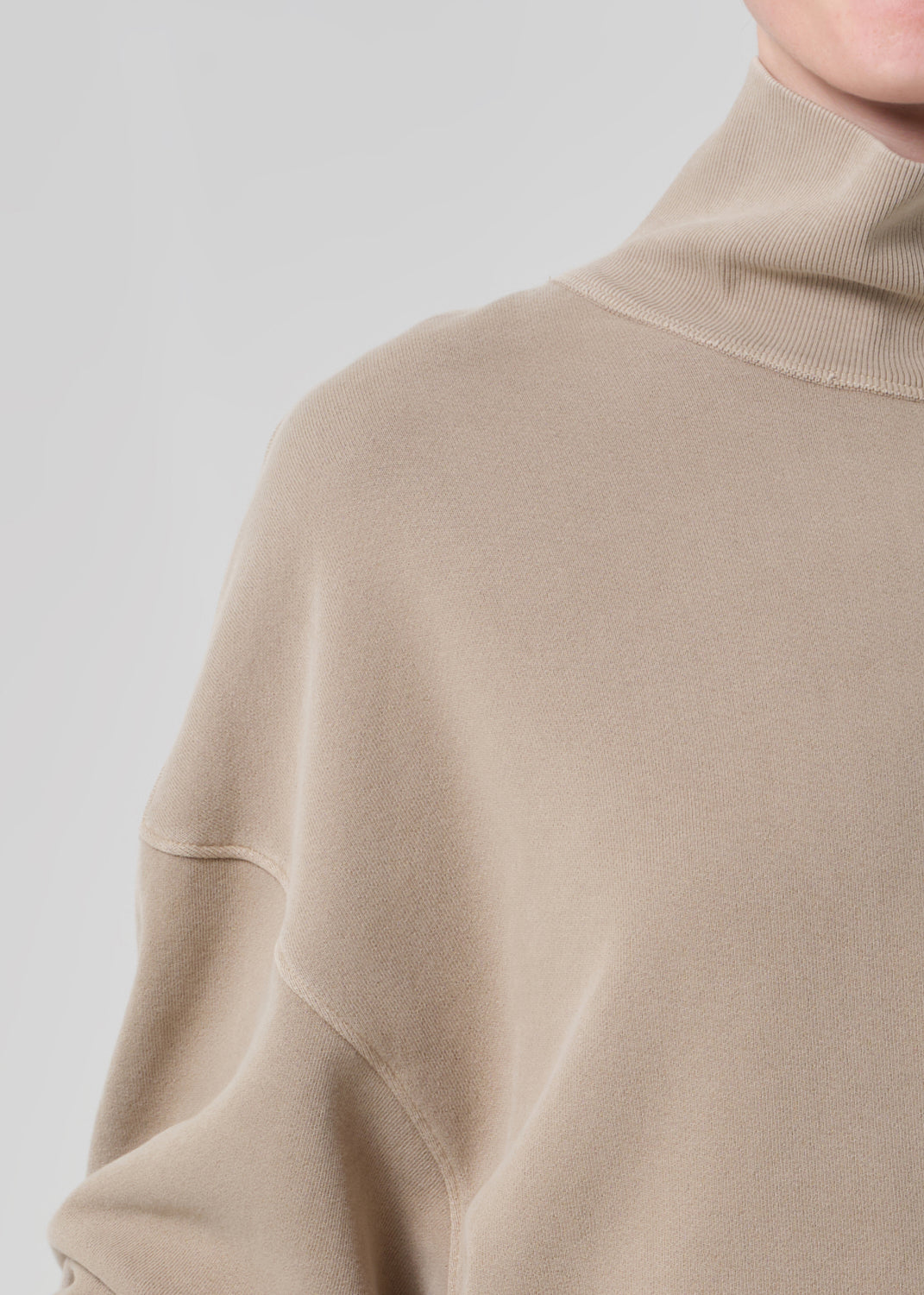 Person wearing a beige turtleneck sweater and pants on a light gray background